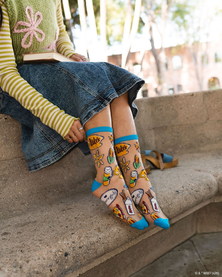 A woman wearing Sock Candy Gilmore Girls Stars Hollow sheer socks with detailed town gazebo and daisy prints.